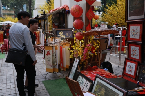 Hai du khách người Hàn Quốc trước gian hàng thư pháp với nhiều sản phẩm đầy màu sắc