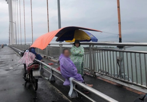 Người mẹ già mặc áo mưa ngồi chờ tìm tung tích con trai trong mưa lạnh.
